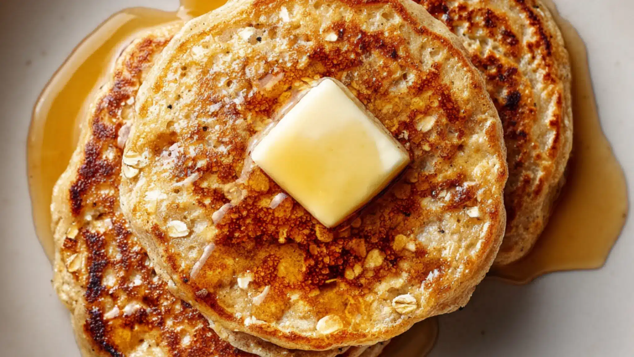 Oat pancakes topped with butter and maple syrup on a plate