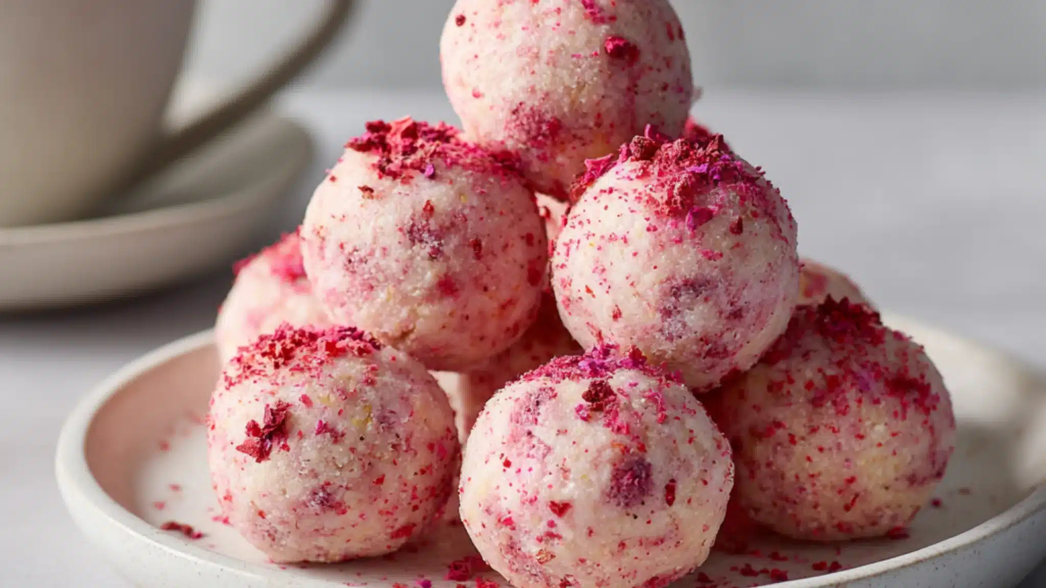 No-bake strawberry cheesecake protein balls stacked on a plate with strawberry topping